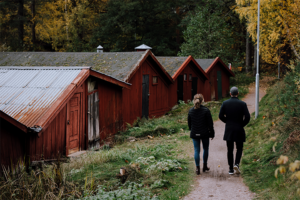 En man och en kvinna promenerar tillsammans på en liten grusväg längs flera rödmålade sjöbodar.
