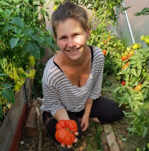 En kvinna visar en stor tomat från tomatodling i växthus