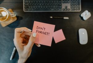 En ljus hand med ljusblått nagellack håller i en rosa post-it lapp där det står "Don't forget"
