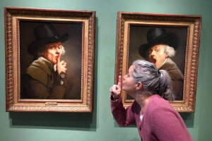 Person på konstmuseum som hyssjar tillbaka åt gubben i målningen som hyssjar med sitt finger på konstmuseum