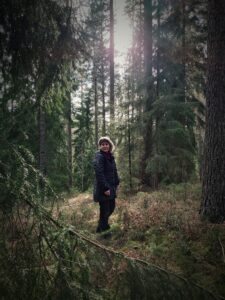 Kvinna står mitt i en skog med granar