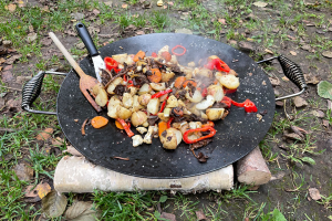 En rykande varm pyttipanna med trattkantareller och grönsaker lagas utomhus på en stekhäll