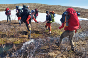 Vandrare på väg över en bäck, en person räcker ut handen för att ta emot en kamrat som ska bege sig över.