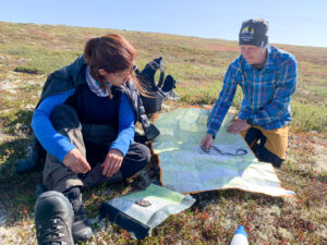 Två personer klädda i outdoorkläder sitter vid en karta på en tundra.