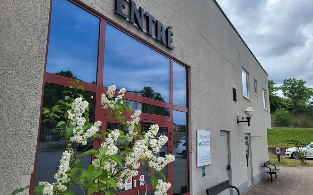 Bild på skolans Entré. En grå byggnad. med en röd dörr med glaspartier. Svart text ovanför med texten "Entré".