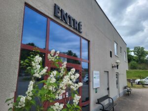 Bild på skolans Entré. En grå byggnad. med en röd dörr med glaspartier. Svart text ovanför med texten "Entré".